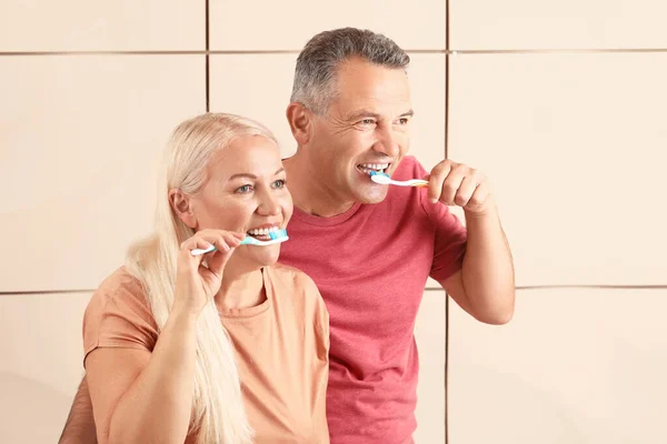 Mature couple brushing teeth on color background — Stock Photo, Image