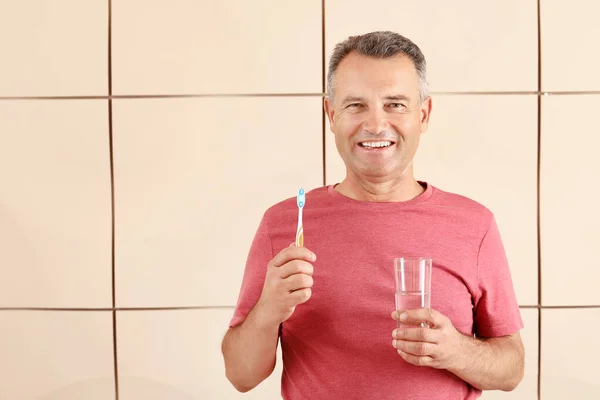 Hombre maduro con cepillo de dientes y vaso de agua sobre fondo de color —  Fotos de Stock