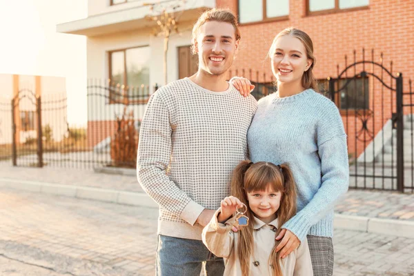 Família jovem com chave perto de sua nova casa — Fotografia de Stock