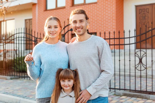 Família jovem com chave perto de sua nova casa — Fotografia de Stock