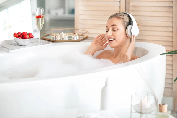 Schöne junge Frau hört Musik im Badezimmer — Stockfoto