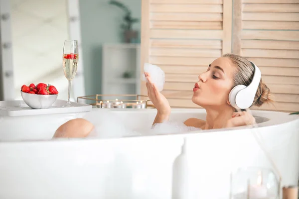 Schöne junge Frau hört Musik im Badezimmer — Stockfoto