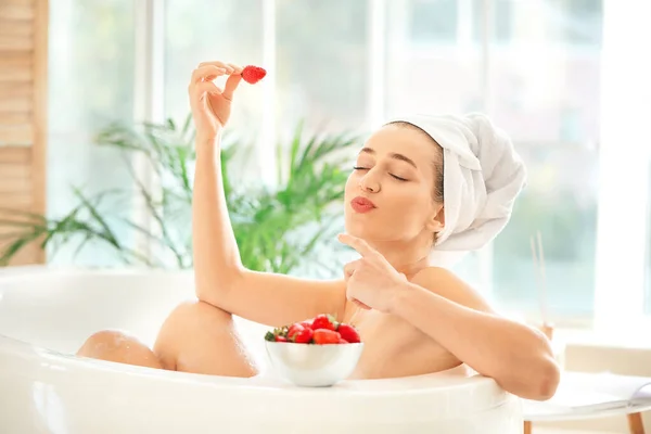 Beautiful young woman eating sweet strawberries in bathroom — Stock Photo, Image