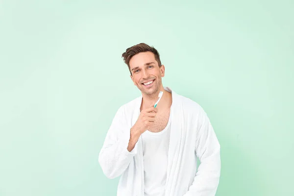 Hombre guapo en albornoz limpiando dientes sobre fondo de color —  Fotos de Stock