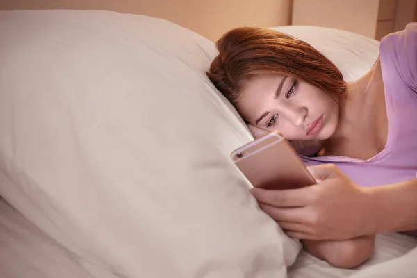 Teenage girl with mobile phone lying in bed at night — Stock Photo, Image