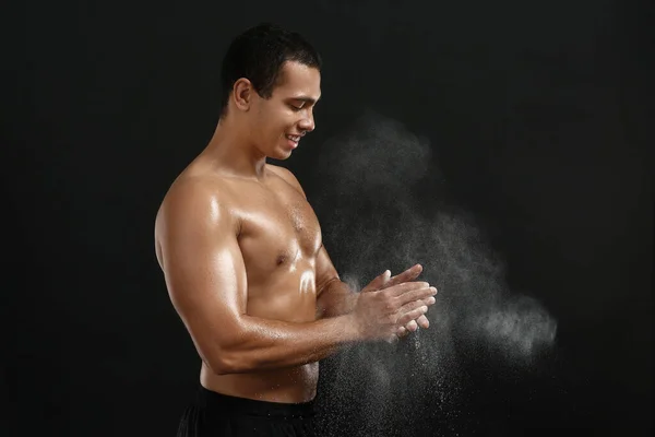 Sporty African-American man applying talc powder on hands against dark background — Stock Photo, Image