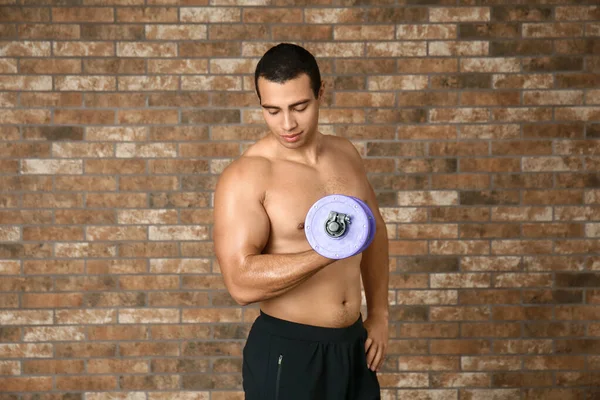 Sporty African-American man with dumbbell on brick background — Stock Photo, Image