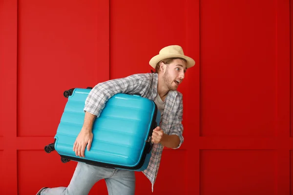 Turista masculino apressando com bagagem contra parede de cor — Fotografia de Stock