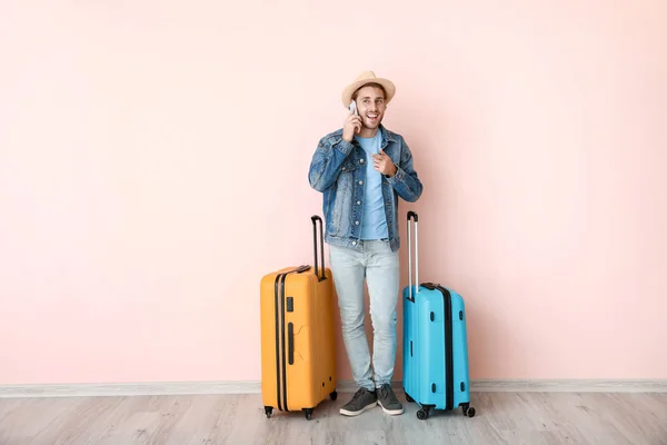 Young male tourist with luggage talking by phone near color wall — 스톡 사진