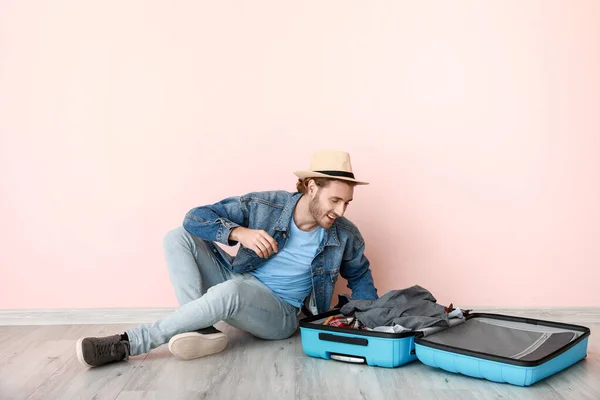 Young male tourist packing suitcase near color wall — Stock Photo, Image