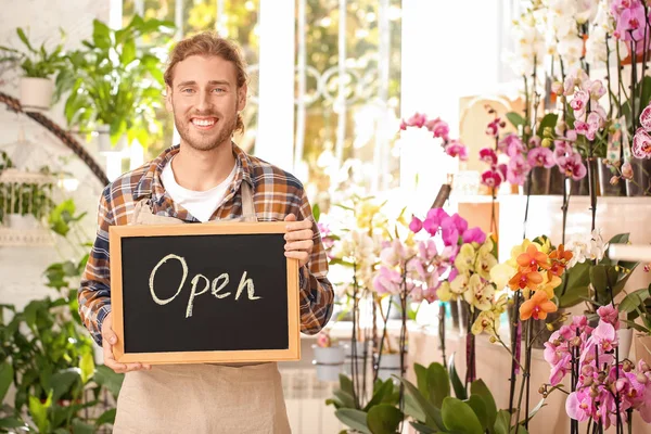 Masculino florista segurando quadro com texto ABERTO na loja — Fotografia de Stock