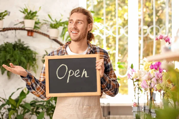 Male florist holding chalkboard with text OPEN in shop — Stock Photo, Image
