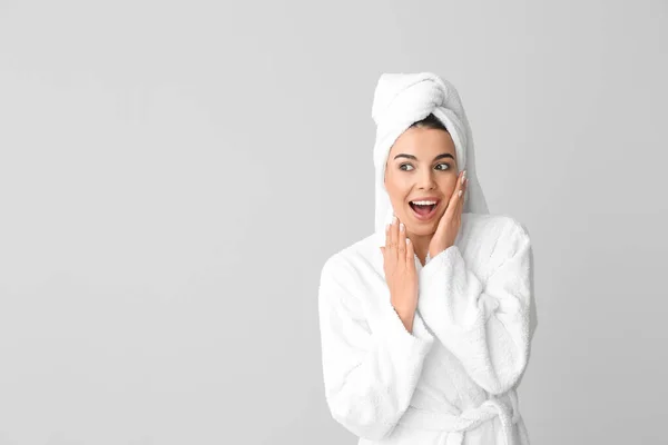 Verrast jonge vrouw in badjas op grijze achtergrond — Stockfoto