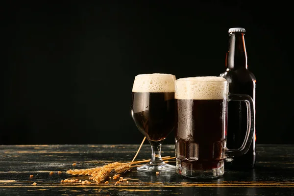 Glassware with fresh beer on table against dark background — Stock Photo, Image