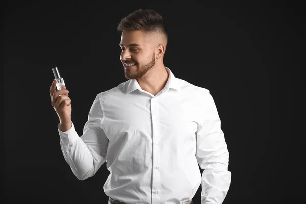 Handsome young man with bottle of perfume on dark background — Stock Photo, Image