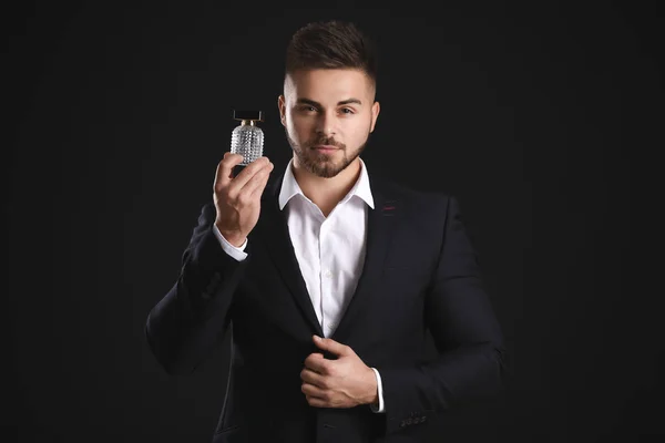 Joven guapo con botella de perfume sobre fondo oscuro —  Fotos de Stock