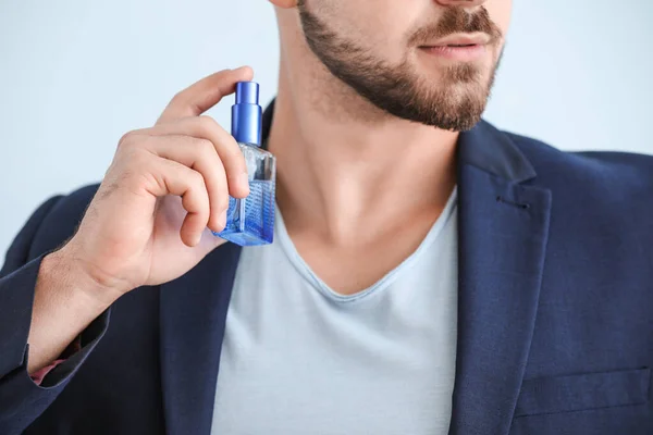 Handsome young man with bottle of perfume on color background, closeup — Stock Photo, Image