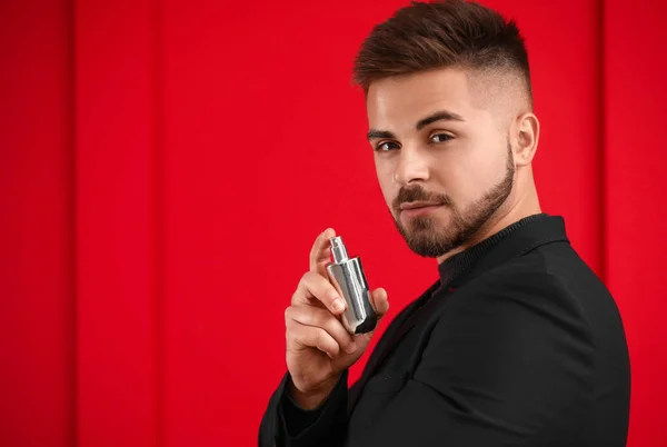 Schöner junger Mann mit einer Flasche Parfüm auf farbigem Hintergrund — Stockfoto