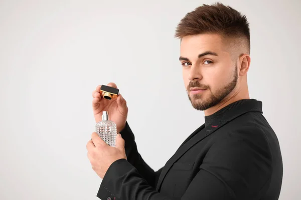 Handsome young man with bottle of perfume on light background — ストック写真