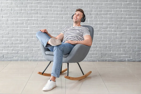 Yakışıklı adam gri duvarın yanında otururken müzik dinliyor. — Stok fotoğraf