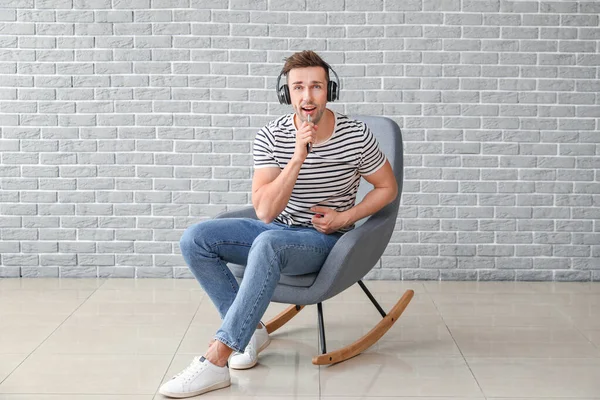 Handsome man listening to music while sitting in armchair near grey wall — Stock Photo, Image