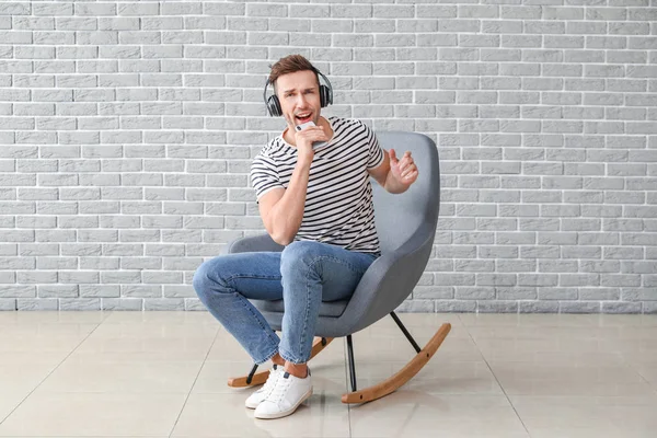 Handsome man listening to music while sitting in armchair near grey wall — 스톡 사진
