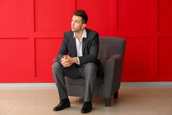 Hombre de negocios guapo sentado en sillón cerca de la pared de color —  Fotos de Stock
