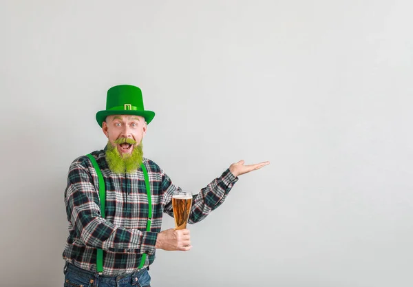 Grappige volwassen man met een glas bier dat iets laat zien op een lichte achtergrond. St. Patrick 's Day viering — Stockfoto