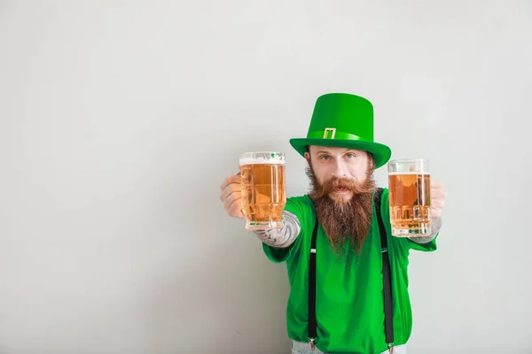 Hombre barbudo con vasos de cerveza sobre fondo claro. Celebración del Día de San Patricio — Foto de Stock