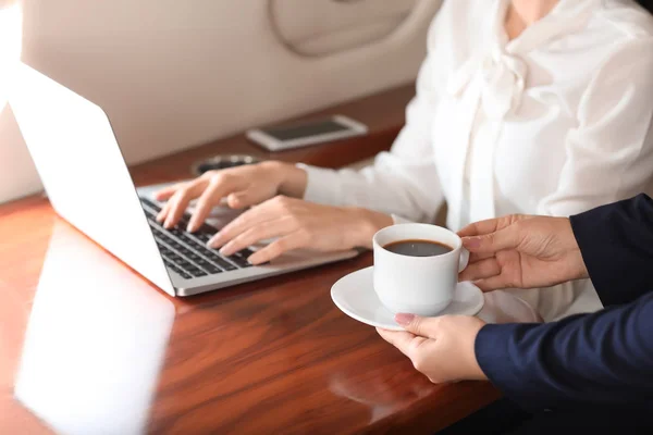 Air hostess bringing coffee for businesswoman on board the modern private airplane