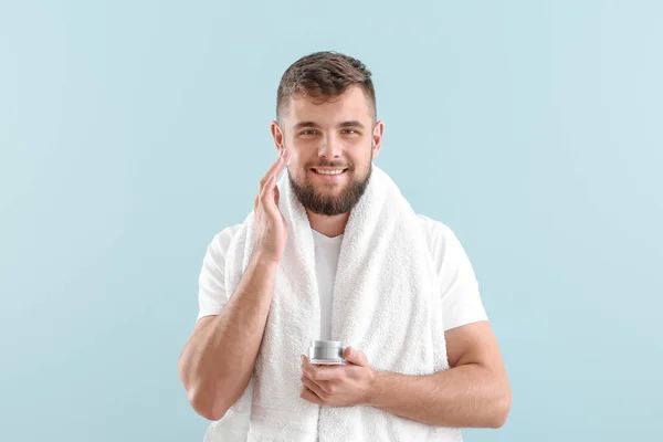 Guapo joven aplicando crema en su cara contra el fondo de color — Foto de Stock