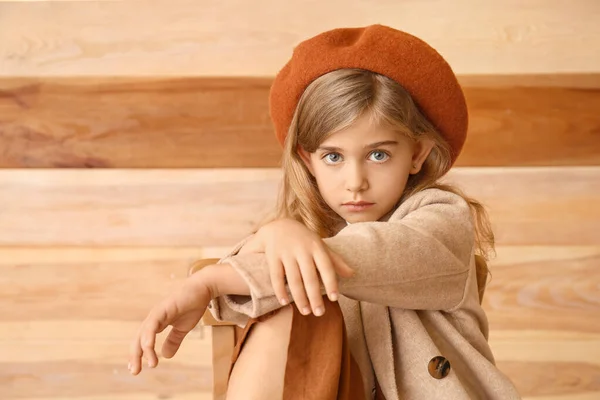 Cute little girl in autumn clothes sitting near wooden wall — 스톡 사진