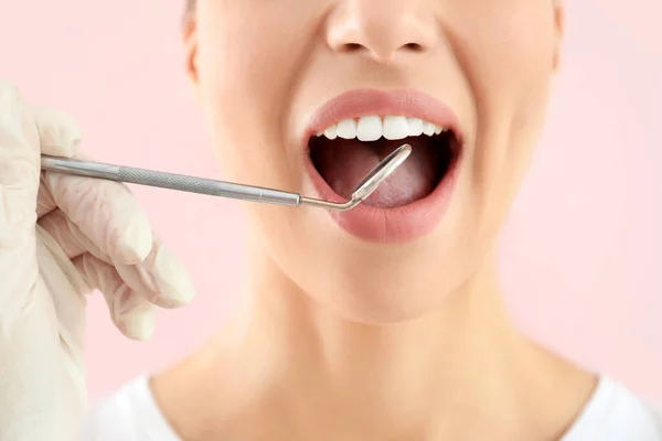 Dentist examining teeth of beautiful young woman against color background — Stock Photo, Image