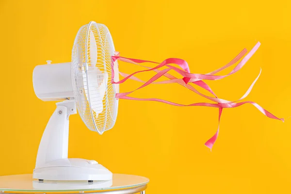 Electric fan with fluttering ribbons on color background — Stock Photo, Image