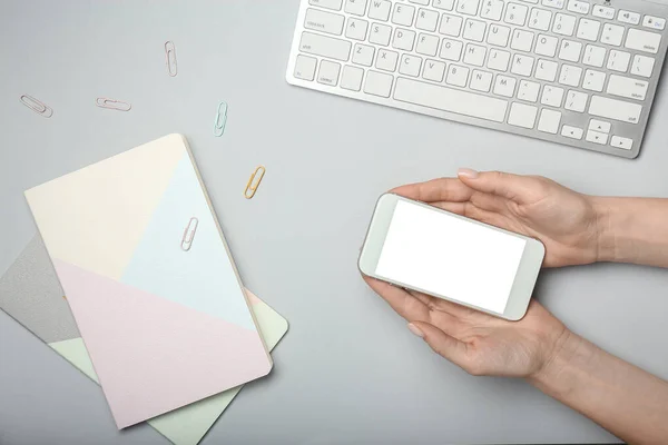 Female hands with mobile phone, PC keyboard and notebooks on light background