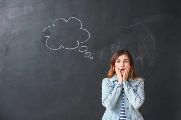 Surprised young woman with blank speech bubble on dark background — ストック写真