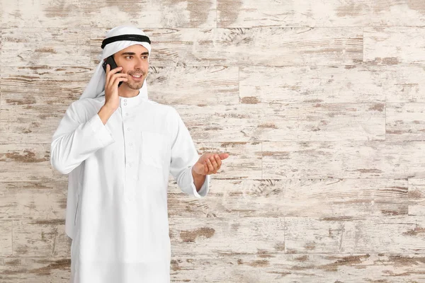 Handsome Arab man talking by phone on wooden background — Stock Photo, Image