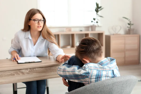 Женщина-психолог работает с грустным мальчиком в офисе — стоковое фото