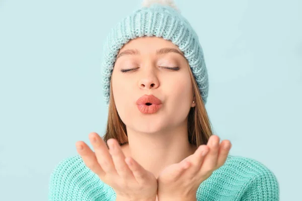 Krásná žena v zimě oblečení foukání polibek na barevném pozadí — Stock fotografie