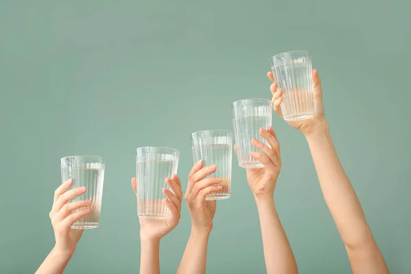 Mãos femininas com copos de água no fundo de cor — Fotografia de Stock