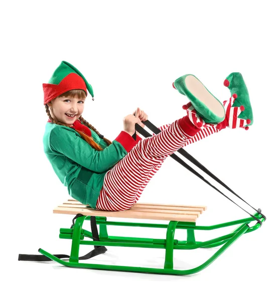 Little girl in costume of elf sitting on sledge against white background — Stock Photo, Image