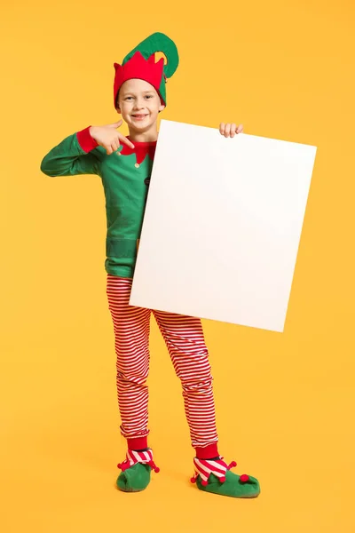 Мальчик в костюме эльфа и с пустым плакатом на цветном фоне — стоковое фото