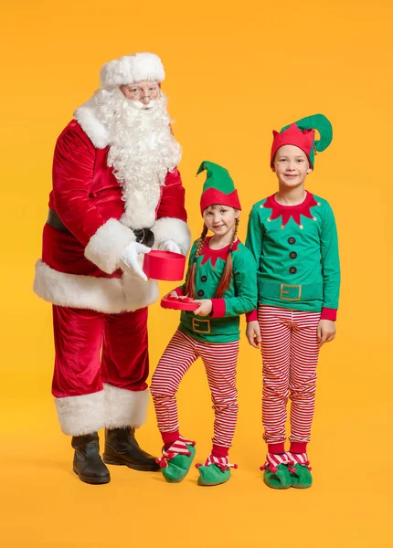 Santa Claus and little elf kids with gift on color background — Stock Photo, Image