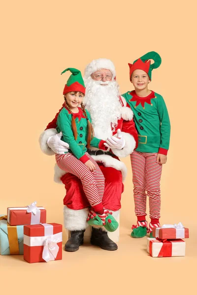Санта-Клаус и маленькие эльфийские дети с подарками на цветном фоне — стоковое фото