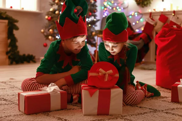 Små barn i dräkt nisse öppning gåva i rum inredda för jul — Stockfoto