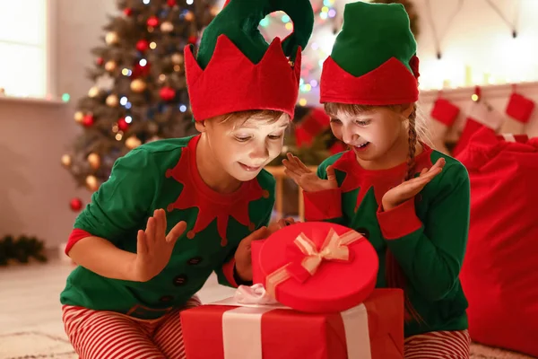 Små barn i dräkt nisse öppning gåva i rum inredda för jul — Stockfoto