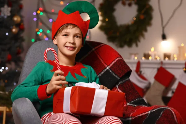 Little boy in costume of elf, with gift and candy cane in room decorated for Christmas — Stock Photo, Image