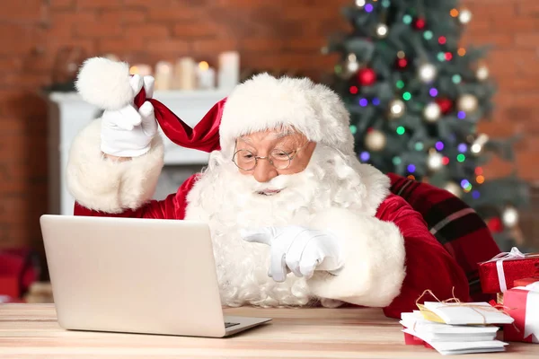 Санта Клаус з ноутбуком перевіряє пошту в кімнаті, прикрашеній на Різдво. — стокове фото