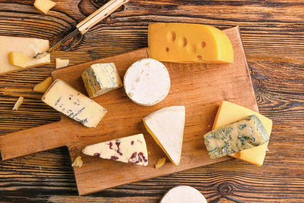 Board with assortment of fresh cheeses on wooden table — Stock Photo, Image