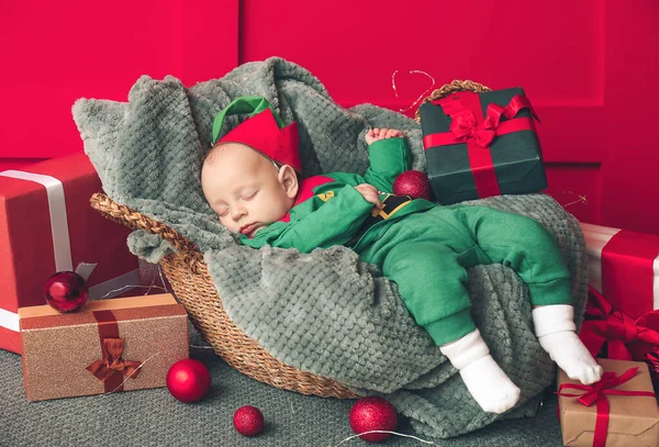 Pequeno bebê em traje de duende e com presentes de Natal dormindo em cesta em casa — Fotografia de Stock